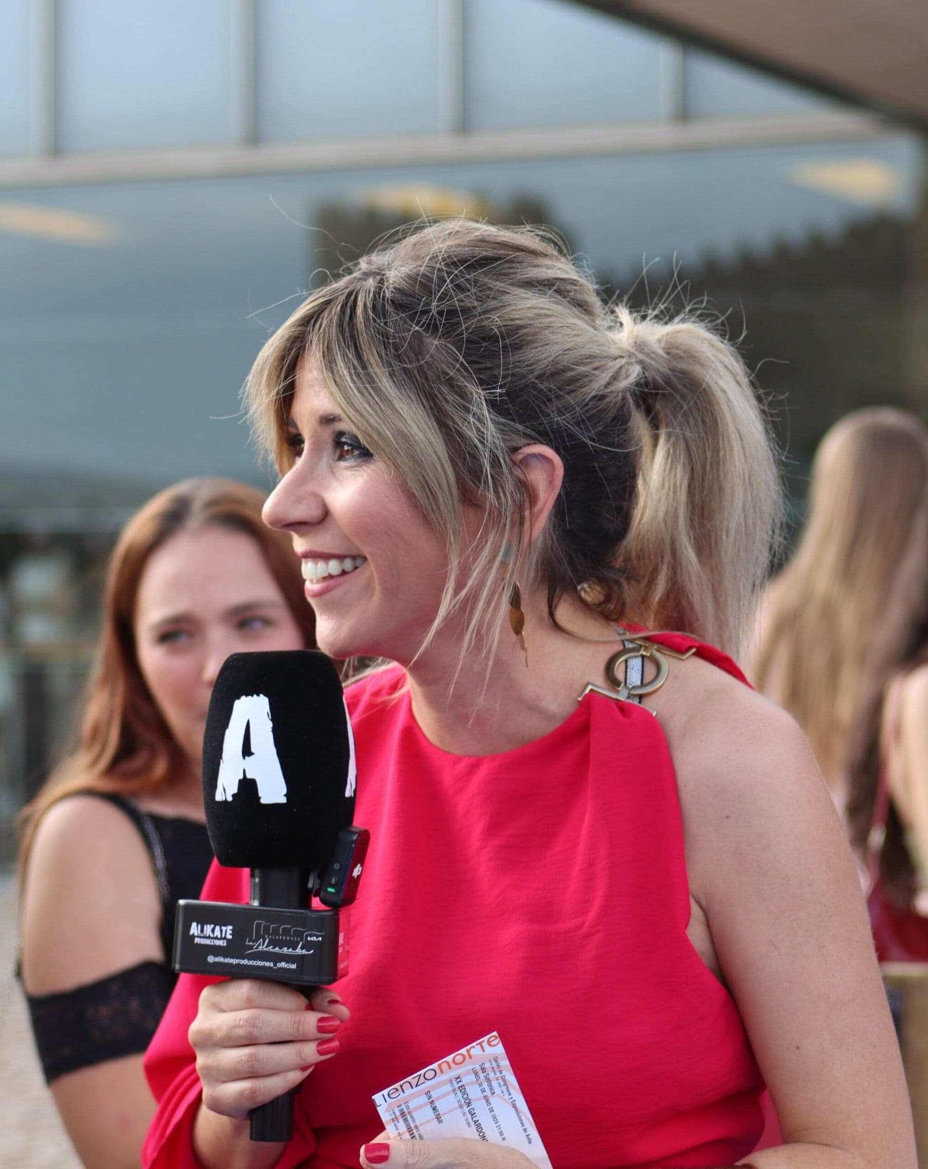 Palo Capilla presentando un evento con micrófono y vestido rojo